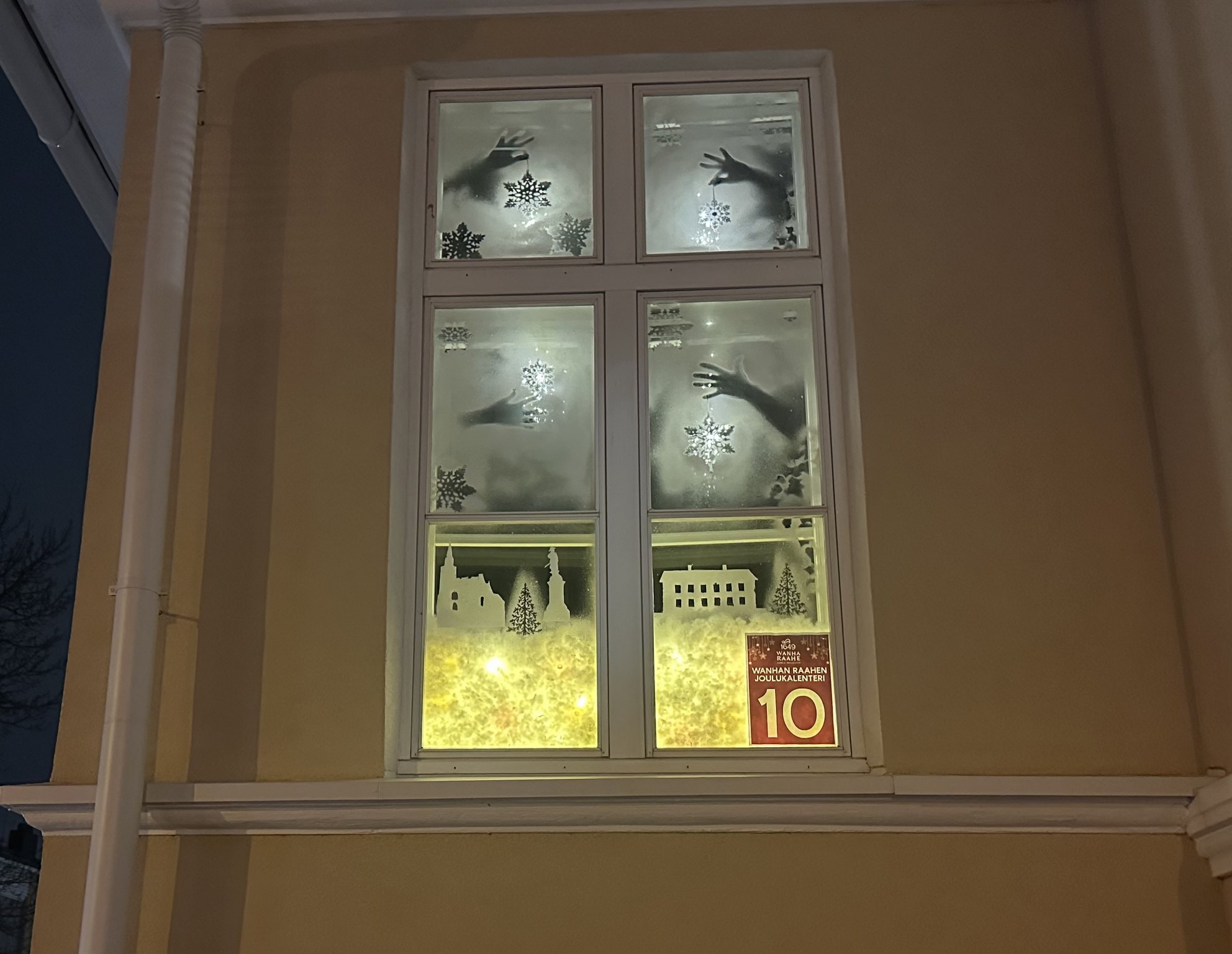 Old Town Raahe Advent Calendar window, where is a winter city scenery and hands holding Christmas ornaments.