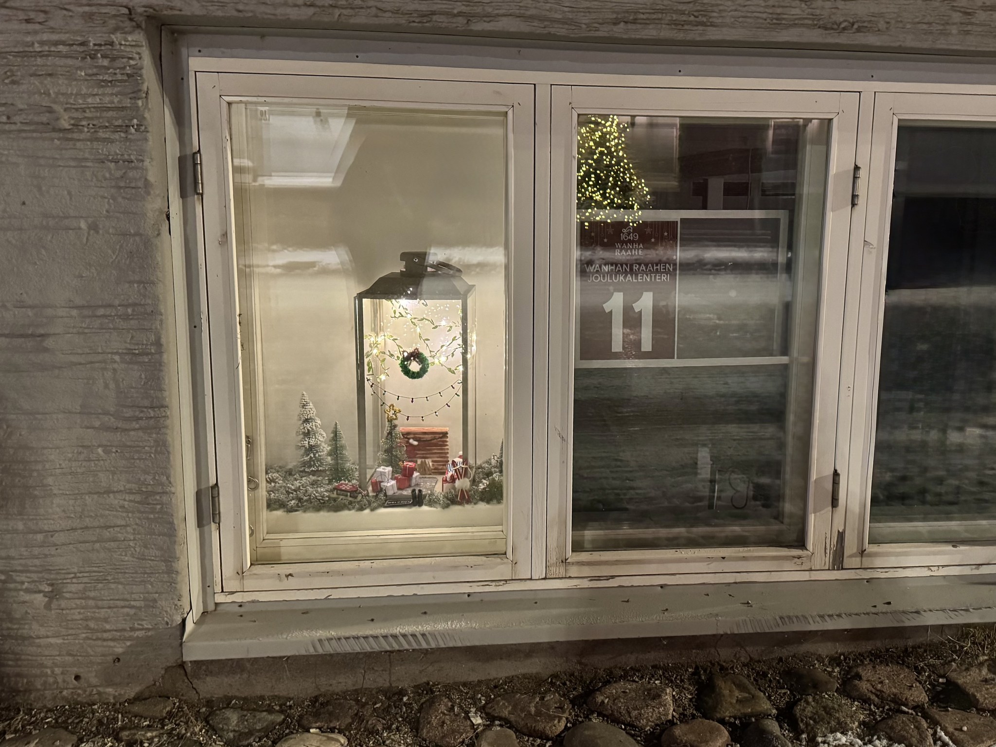 Wanhan Raahen joululalenterin ikkuna, jossa talvinen maisema ja jouluinen koti lyhdyn sisällä.