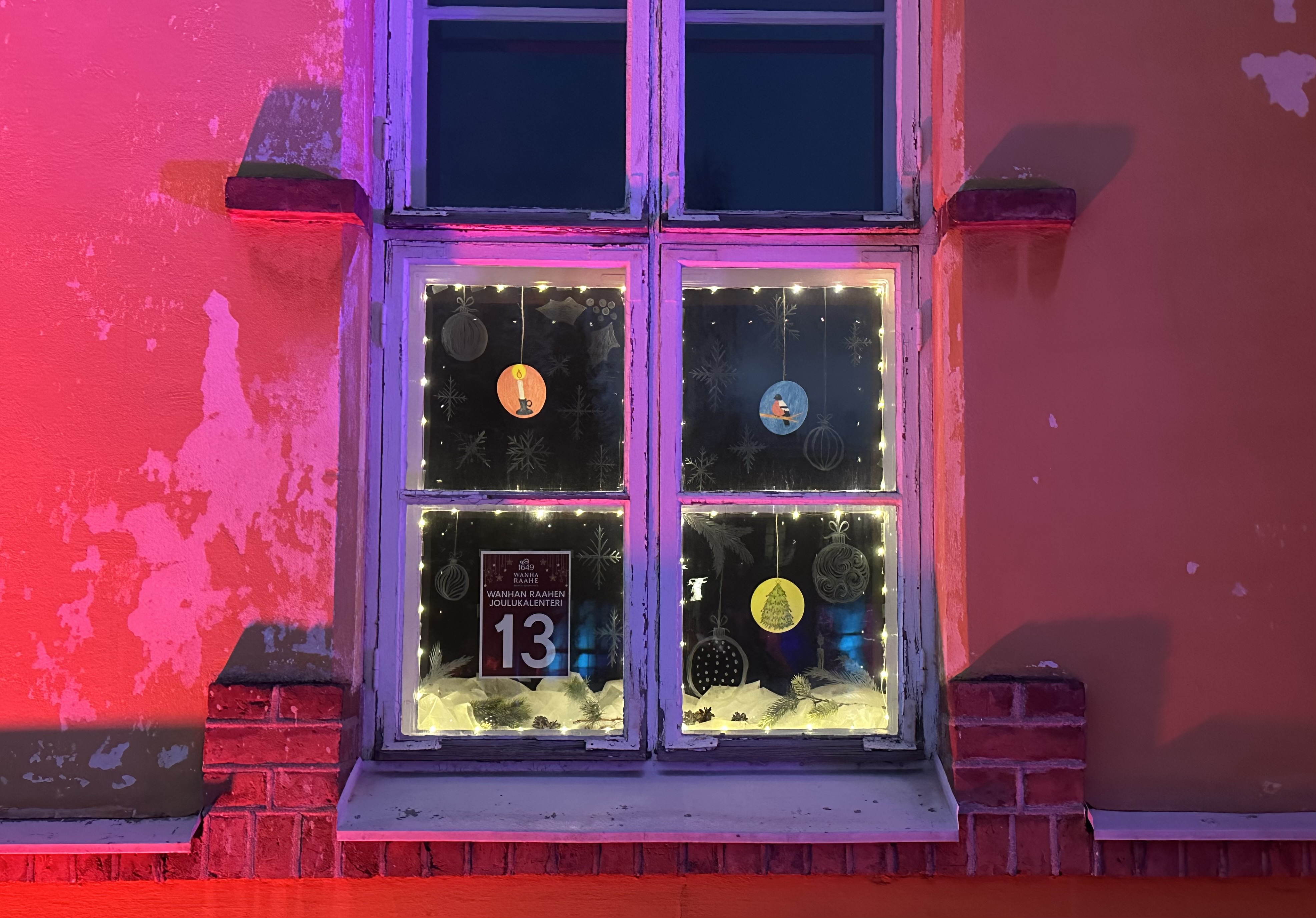 Wanhan Raahen Joulukalenteri luukku 13. Ikkunassa on paperisia, kuvitettuja joulupalloja roikumassa sekä piirrettyjä joulupalloja.
