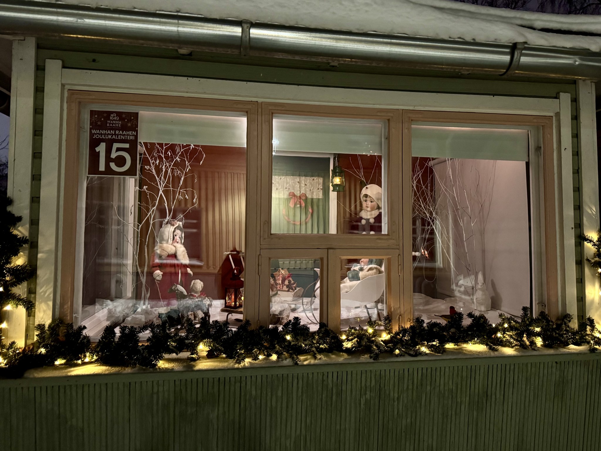 Wanhan Raahen joulukalenterin ikkuna, jossa lapsi reen kyydissä kahden muun lapsen katsoessa.