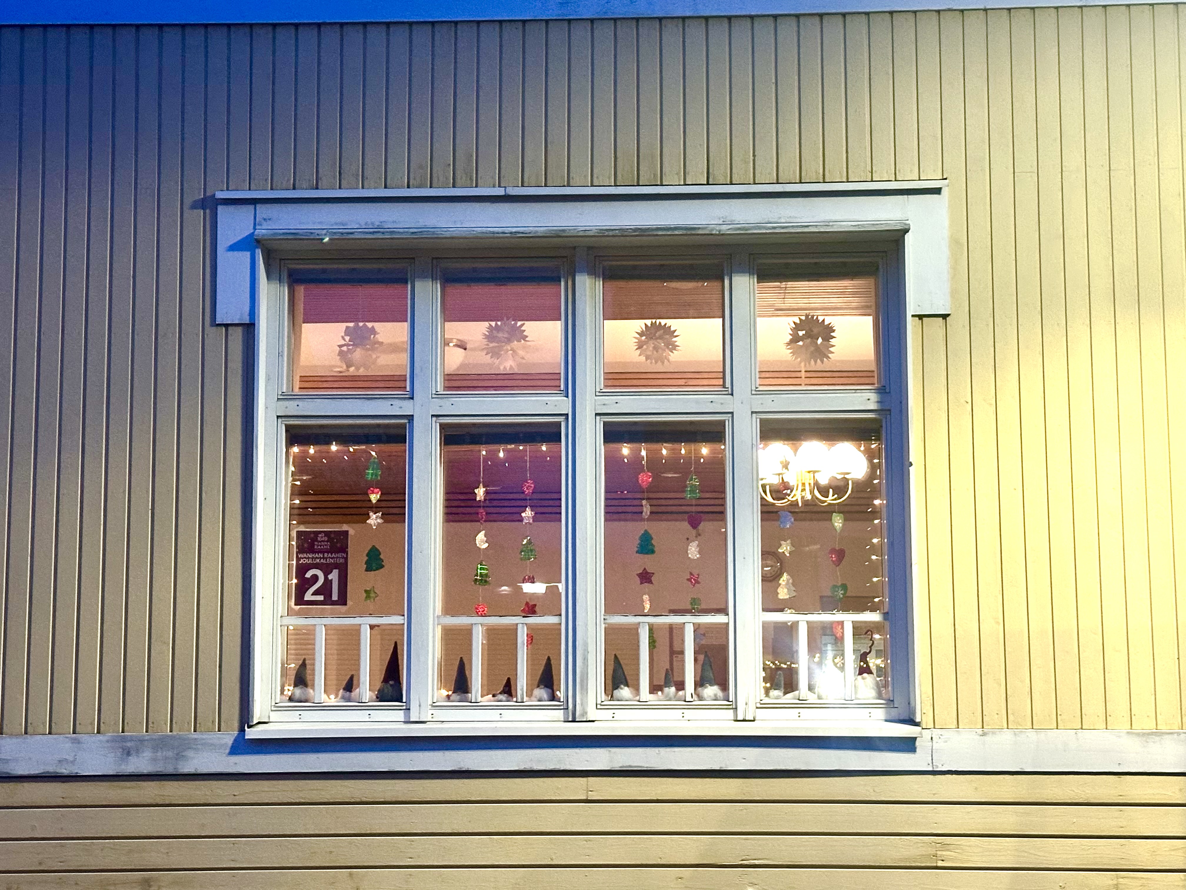 Luukku 21, paperisia lumitähtiä ja valoja ikkunassa.