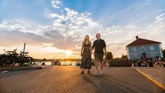 Pariskunta Raahen museonrannassa auringonlaskussa, taustalla näkyy Pakkahuoneen museo.