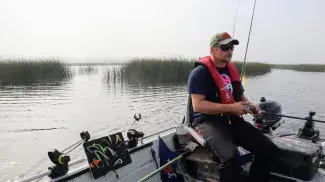 Kalastaja istuu veneessä vieressään erilaisia kalastusvälineitä